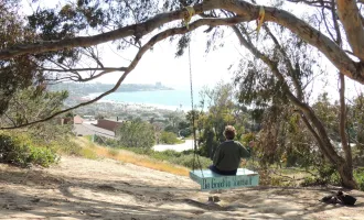 Woman sitting on a swing looking out towards the ocean.