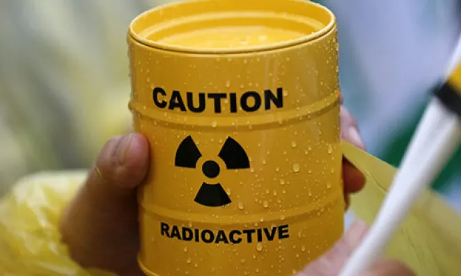 Hand holds canister with radioactive sign.