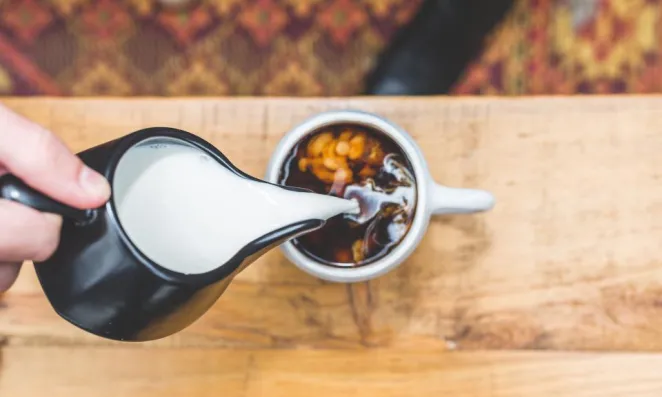 Milk pouring in cup of coffee.