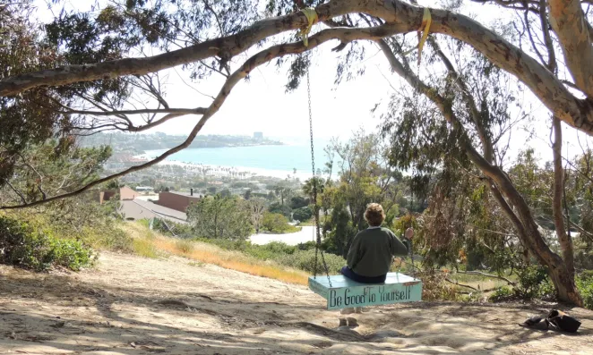 Woman sitting on a swing looking out towards the ocean.