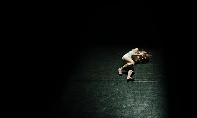 Woman clutching head laying on a floor.