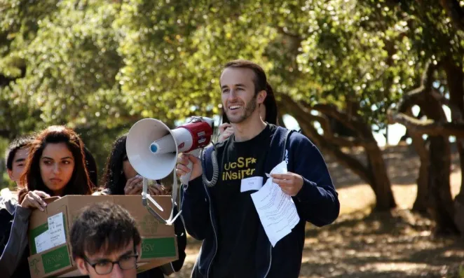 student smiling with a bullhorn, other students around