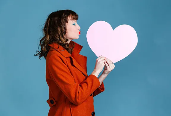 Woman kissing cardboard cutout of a heart.