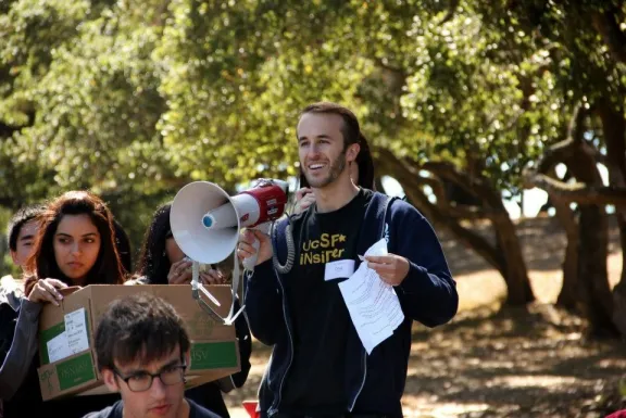 student smiling with a bullhorn, other students around